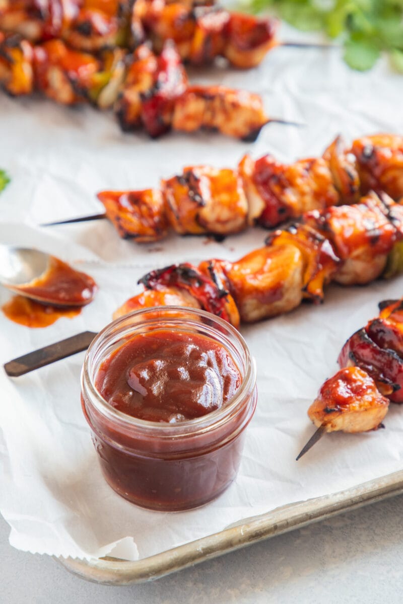 Guava BBQ Sauce in a jar with chicken skewers in the back