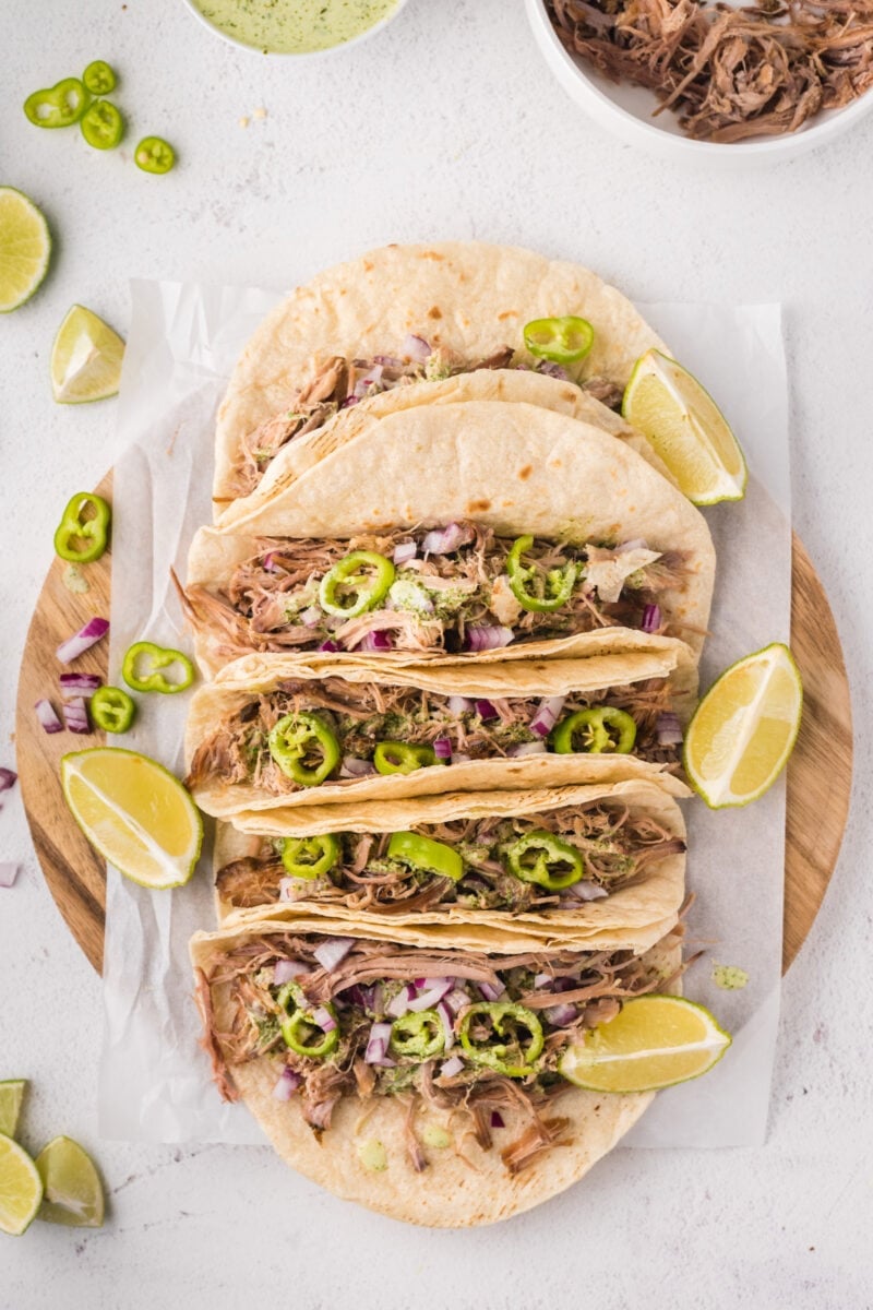 Overhead shot of five tacos on a wooden chopping board