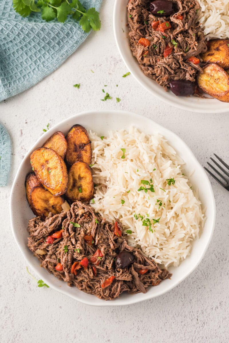 Carne de res deshebrada servida en dos tazones con arroz y plátano