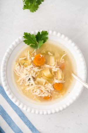 Chicken noodle soup served in a white bowl with fresh cilantro.