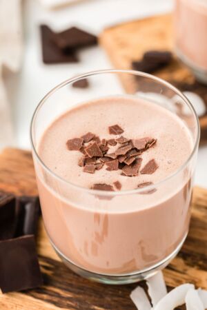 A glass of coquito topped with chocolate flakes.