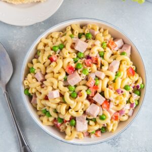Pasta salad with peas and ham served in a white bowl.