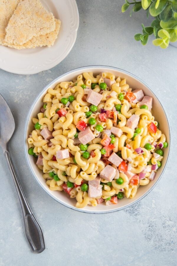 Pasta salad with peas and ham served in a white bowl.