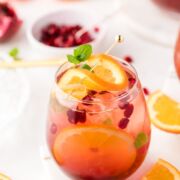 A glass of sangria next to slices of oranges and pomegranate seeds.