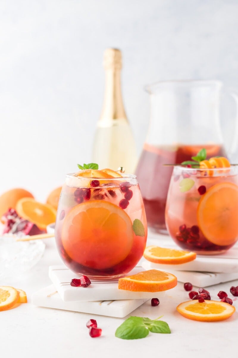 Two glasses of pomegranate sangria in front of a wine bottle and a pitcher.