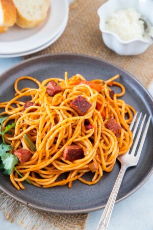 Dominican Spaghetti served on a grey plate with a side of bread and Parmesan cheese