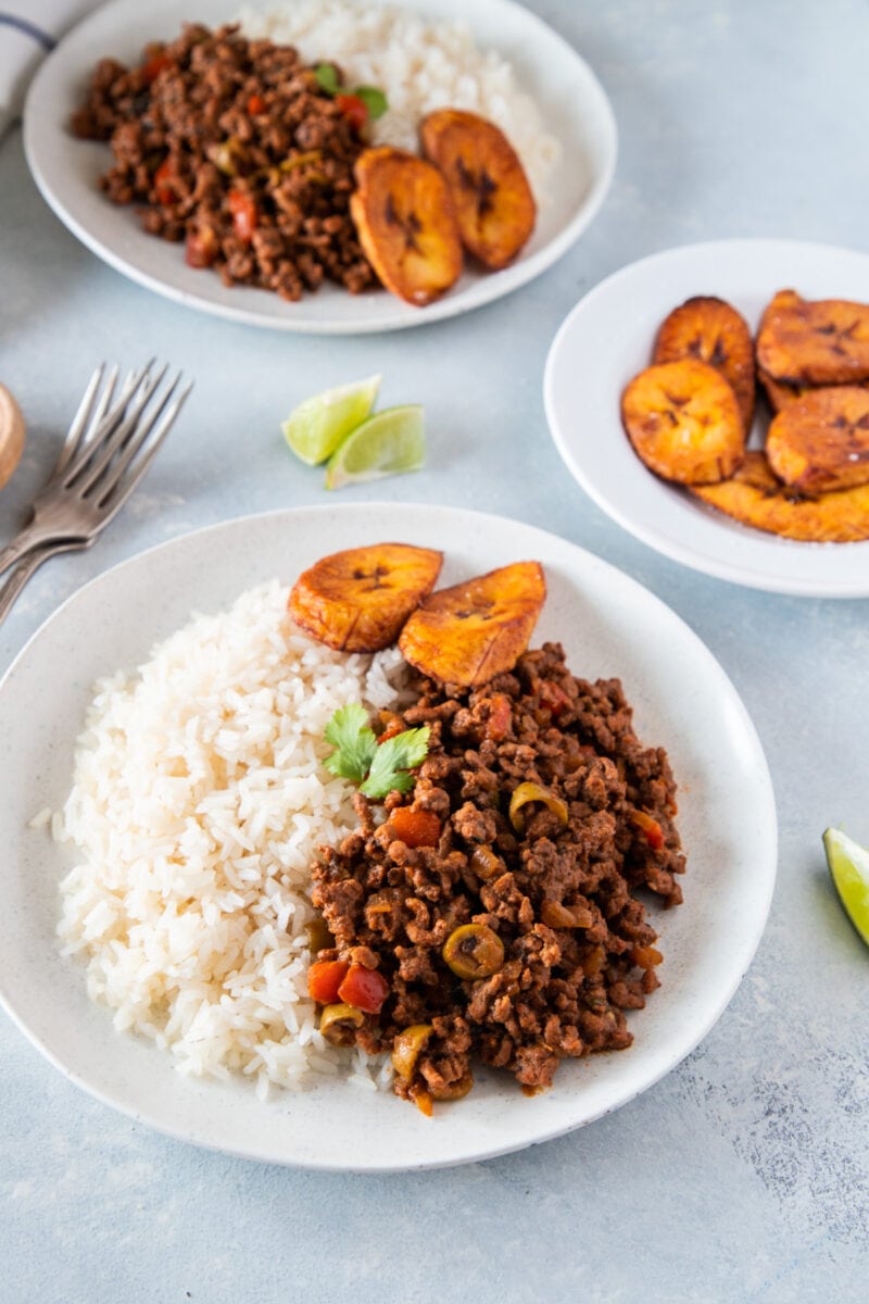 Two plates of Picadillo served with rice and plantains
