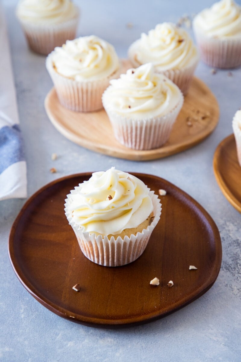 almond cupcakes with cream cheese frosting on a wooden plate