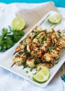 chicken skewers served on a white platter with lime wedges on the side and cilantro for garnish