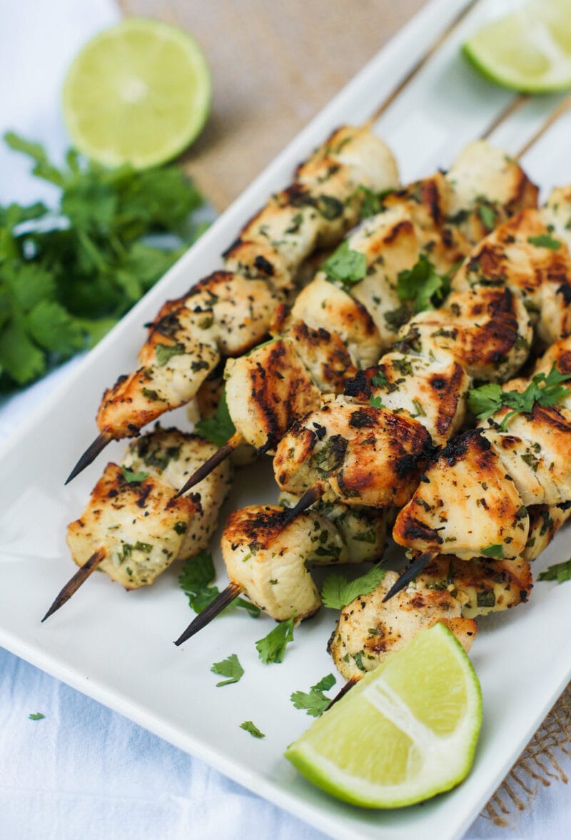 close up of chicken skewers served on a white platter with lime wedges on the side