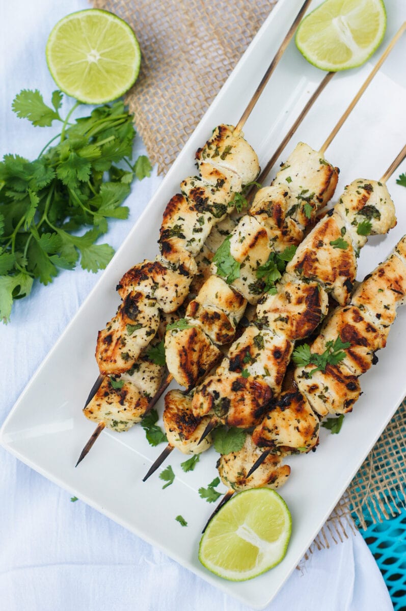 Chicken skewers served on a white plate with lime wedges on the side