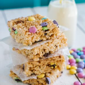 Stacked M&M rice krispies squares with a cup of milk on the side