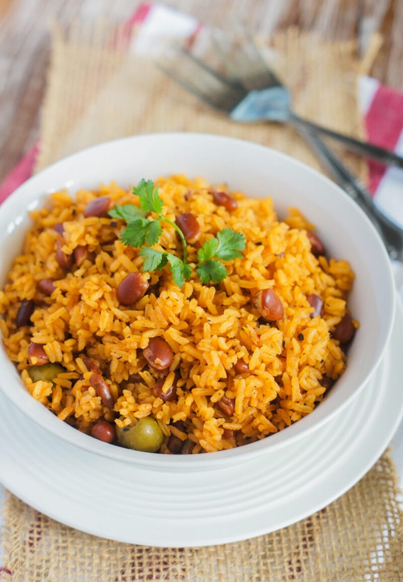 Rice with beans served on a white bowl and topped with cilantro leaves.