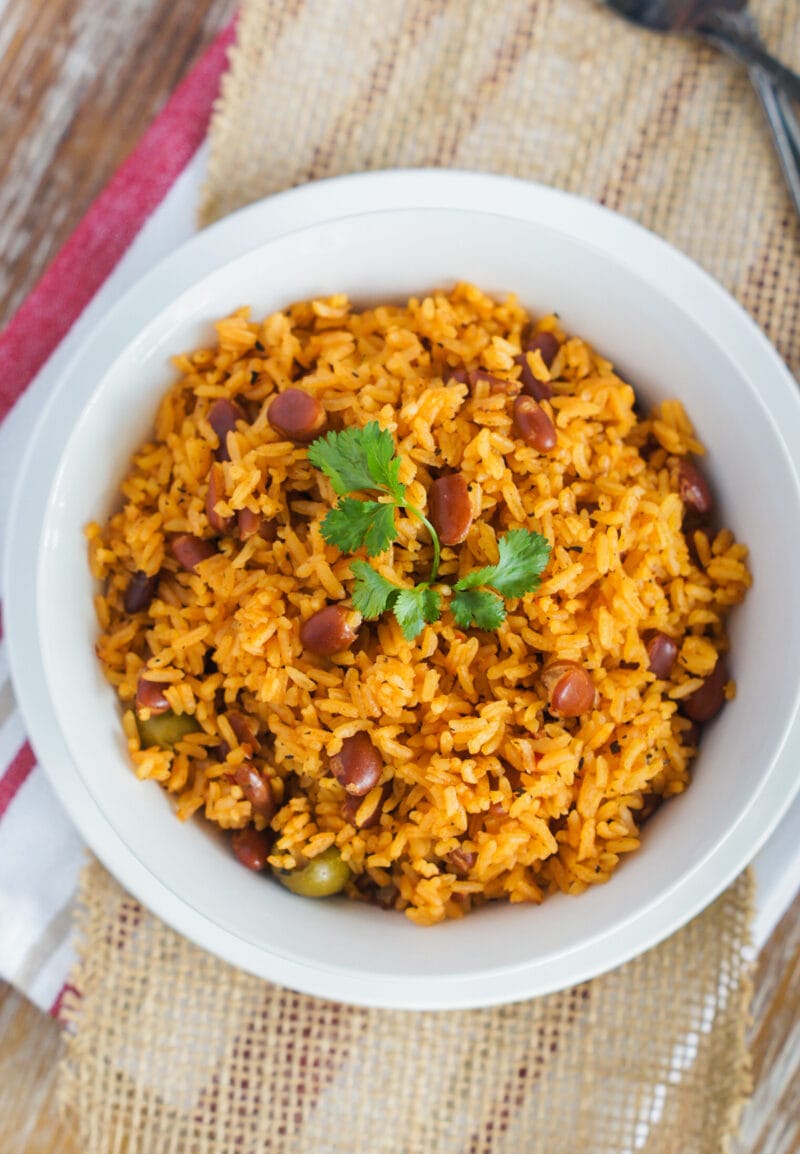 Rice with beans served on a white bowl and topped with cilantro leaves.