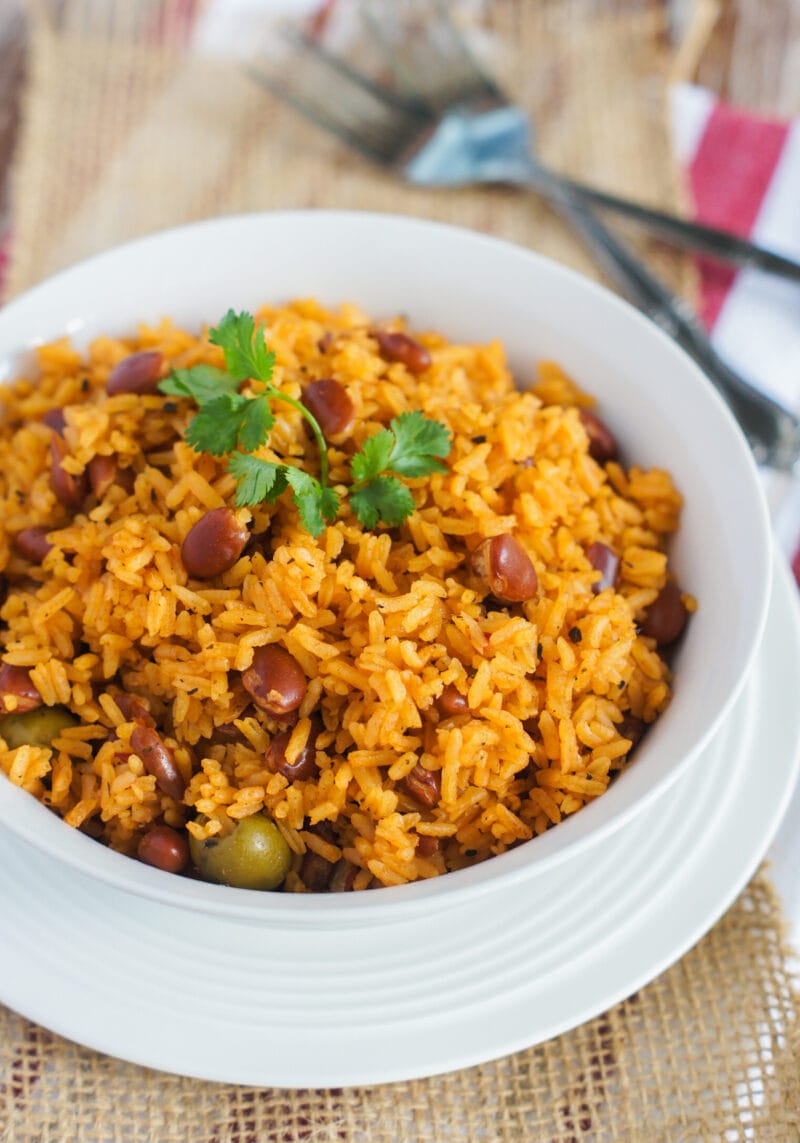 Rice with beans served on a white bowl and topped with cilantro leaves.