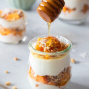 drizzling honey over a glass of papaya yogurt parfait
