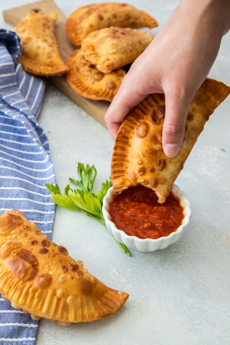 hand dipping empanada in marinara sauce