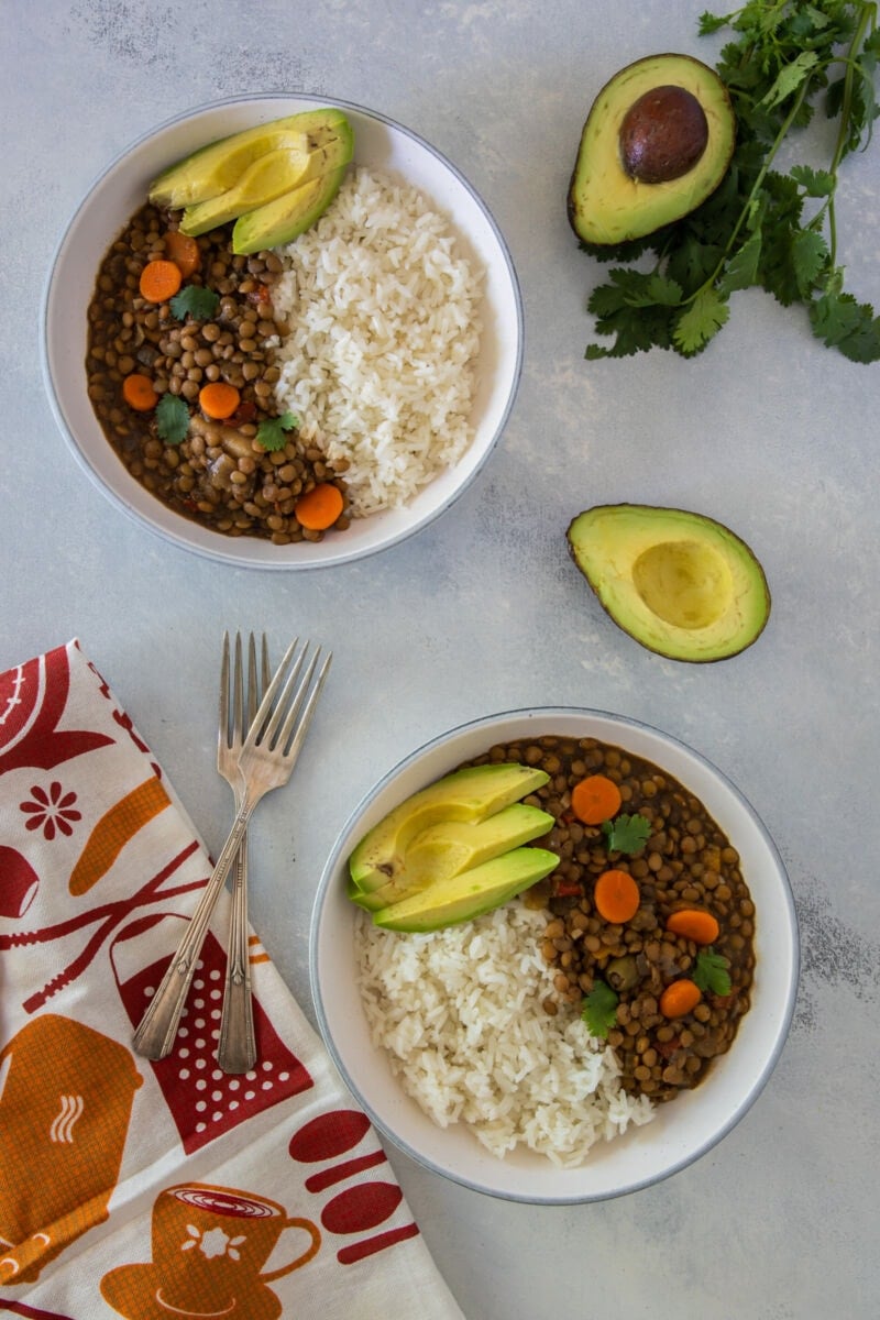 Slow cooker lentil stew served in two bowls with rice and sliced avocado.