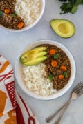 Lentil stew on a plate served with rice and avocado.