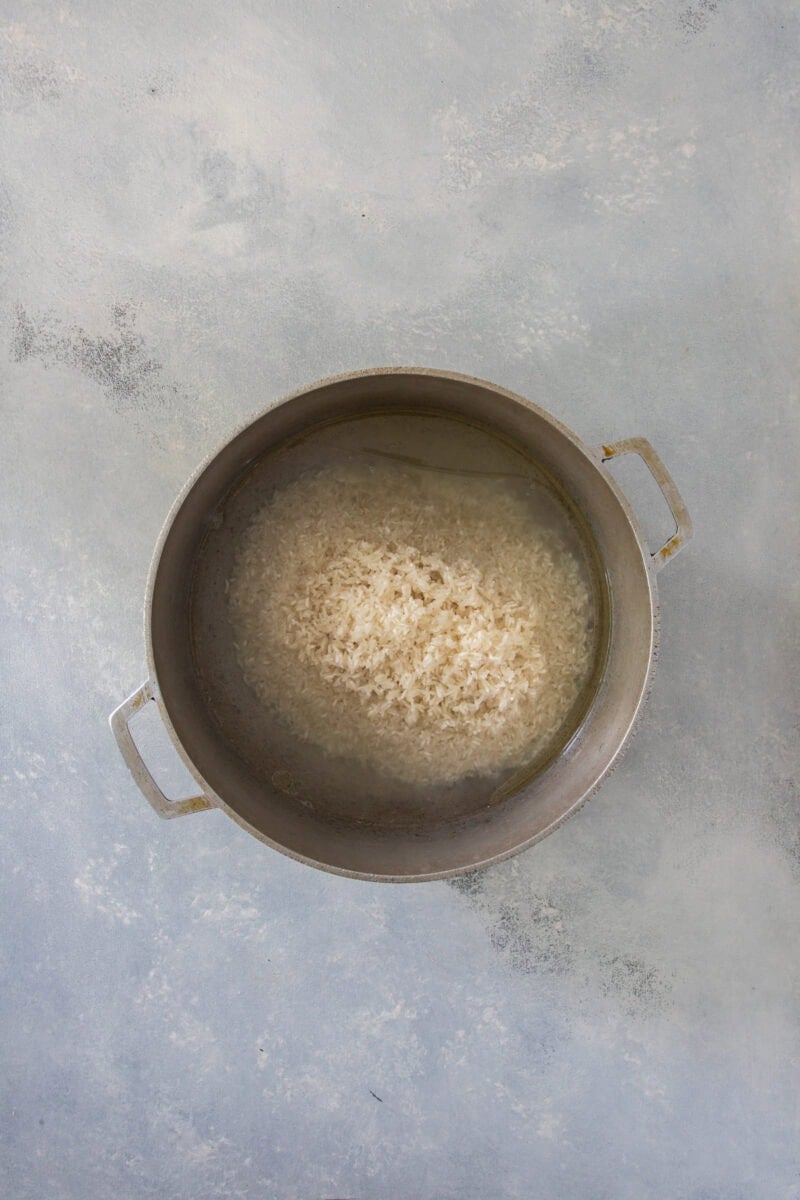 White rice soaking in water in a pot, top view.