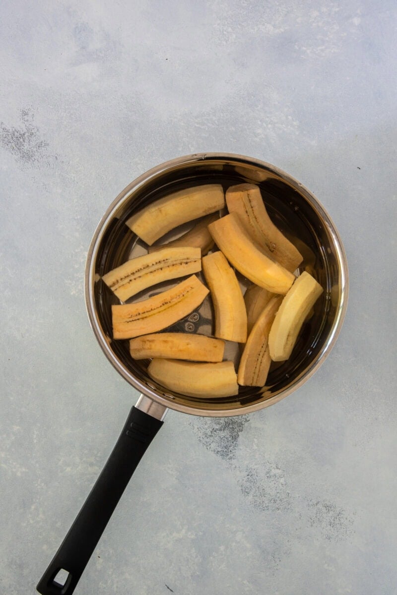 Peeled green plantains cut into chunks in a pot of water.