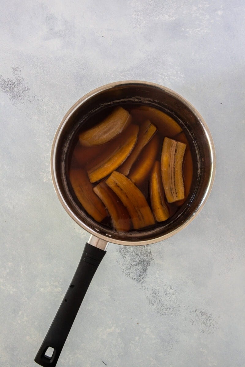Peeled green plantains cut into chunks in a pot of water.