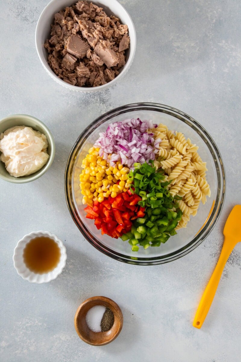 Ingredients for tuna pasta salad in a bowl, including rotini, tuna, corn, red onion, bell peppers, and mayo.