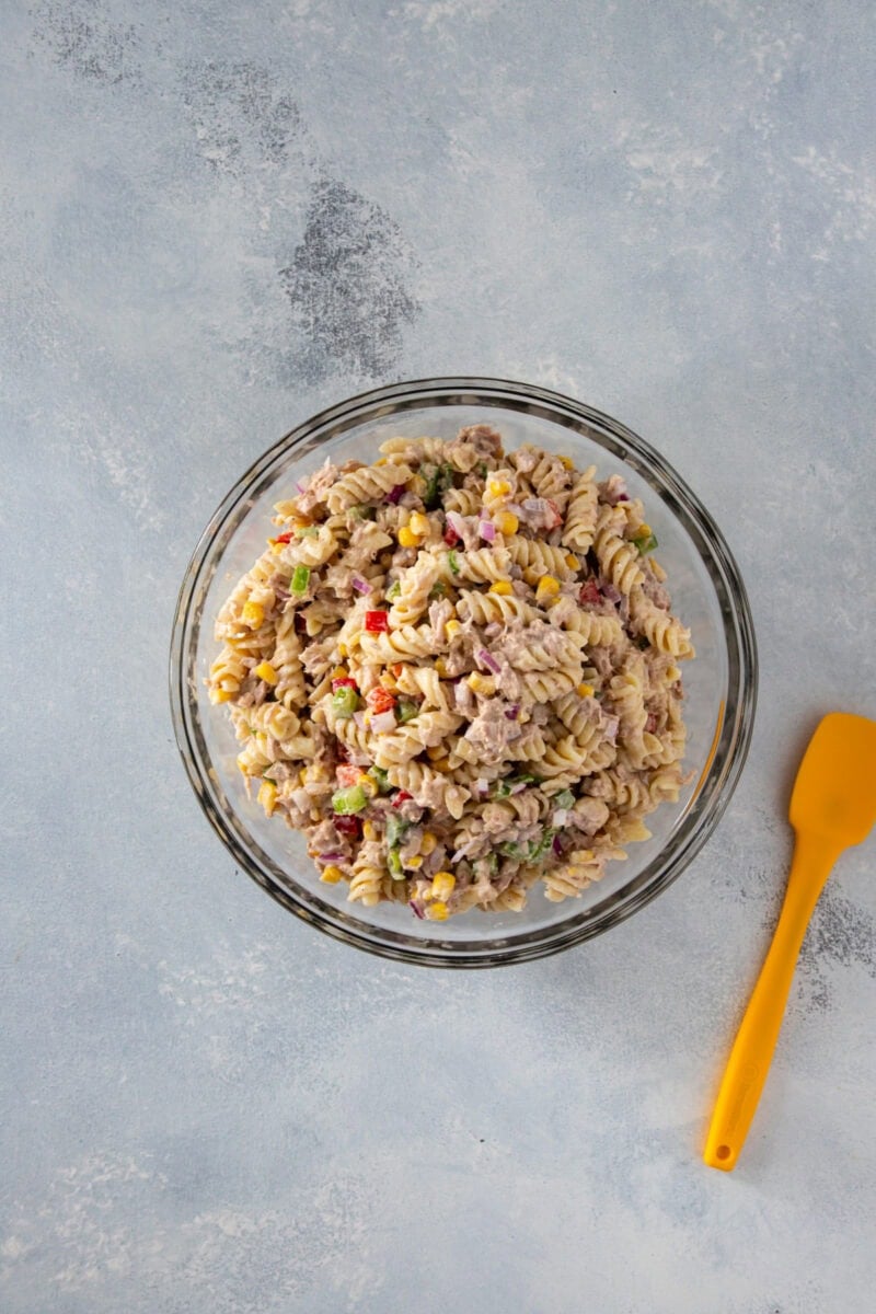 Creamy tuna pasta salad with rotini, corn, and vegetables in a glass bowl.