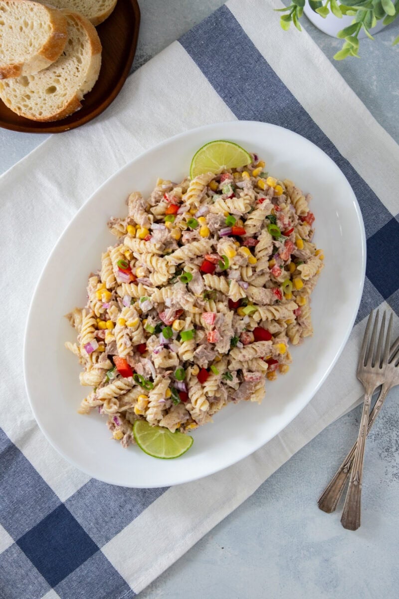 Creamy tuna pasta salad with rotini, vegetables, and corn, served on a dark plate with sliced bread.