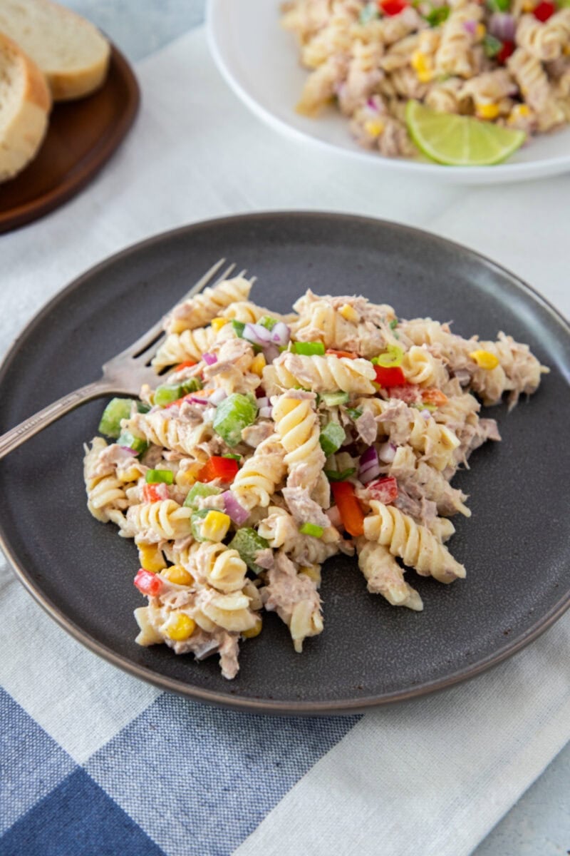 Creamy tuna pasta salad with rotini, vegetables, and corn, served on a dark plate.