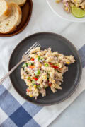 Creamy tuna pasta salad with rotini, vegetables, and corn, served on a dark plate with sliced bread.