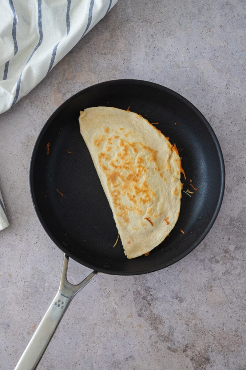 cooking the quesadilla in a pan to melt the cheese