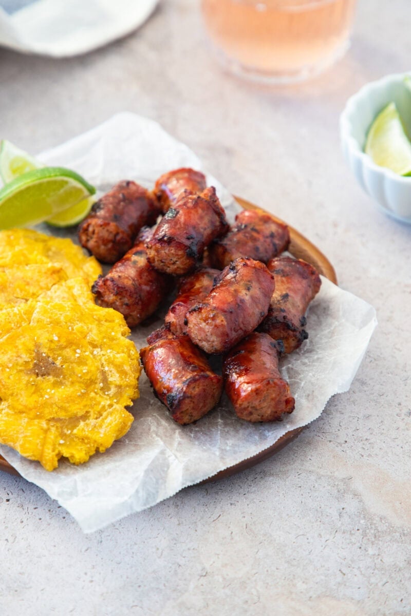 Longaniza frita y tostones en un plato forrado con papel manteca, acompañados de gajos de lima.