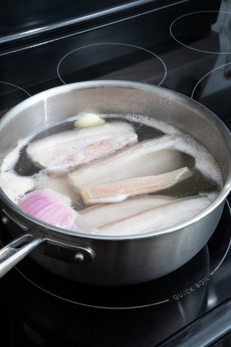 Boiling pork belly with onion and garlic for flavor and tenderness.