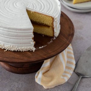 Dominican vanilla cake with dulce de leche filling and white meringue frosting on a wooden stand.