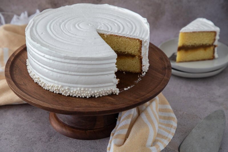 Dominican vanilla cake with dulce de leche filling and white meringue frosting on a wooden stand.