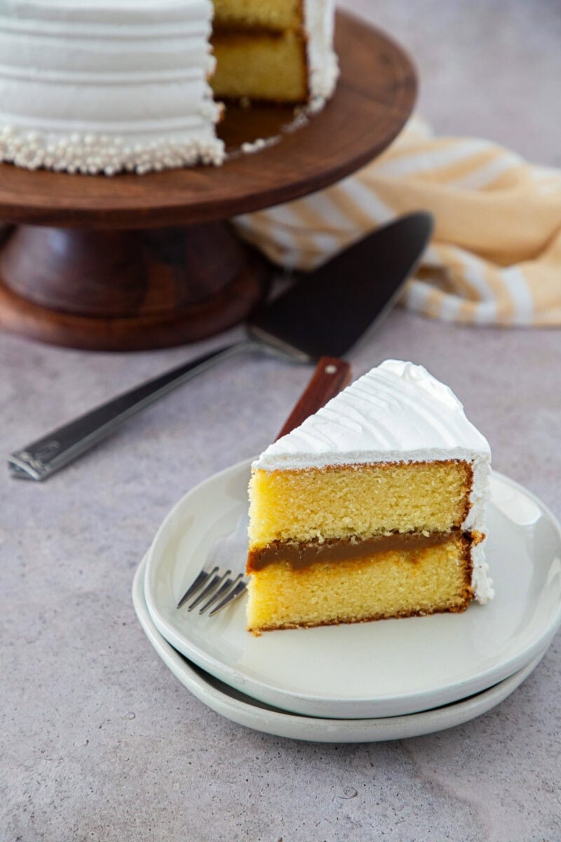 Slice of Dominican cake with dulce de leche filling and white meringue frosting on a plate.