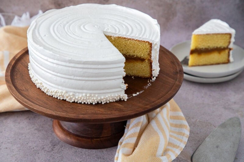Dominican cake with dulce de leche filling and white meringue frosting on a wooden stand.