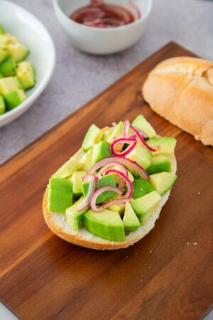 Avocado toast with red onion on rustic bread, served on a wooden board.