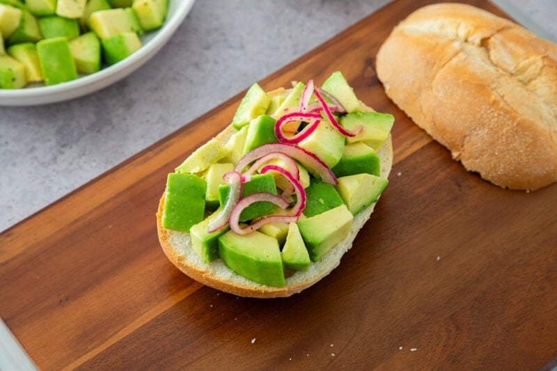 Tostada de aguacate con cebolla roja sobre pan rústico, servida en una tabla de madera.