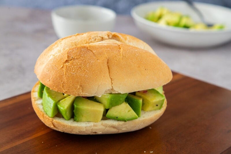 Sándwich de aguacate en pan crujiente, relleno de trozos de aguacate fresco.