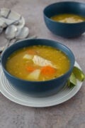 Dominican chicken soup with yuca, carrots, and tender chicken, served in a blue bowl with lime wedges.