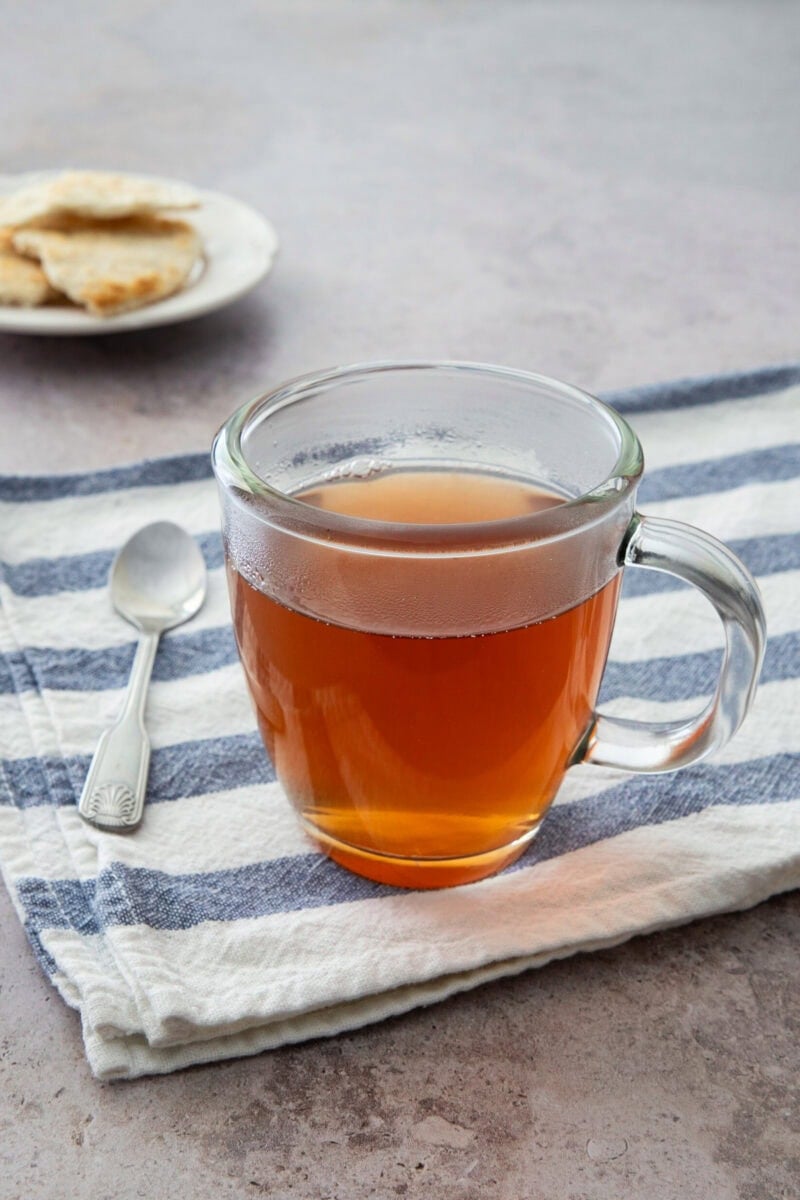 Té de jengibre y canela en una taza de cristal sobre un paño a rayas con una cuchara.