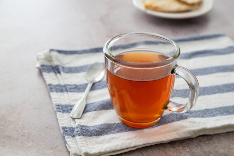 Té caliente de jengibre y canela en una taza transparente con pan plano al fondo.