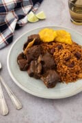 Plate of Dominican stewed goat served with moro rice and fried tostones.