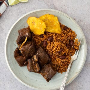Plate of Dominican stewed goat served with moro rice and fried tostones.