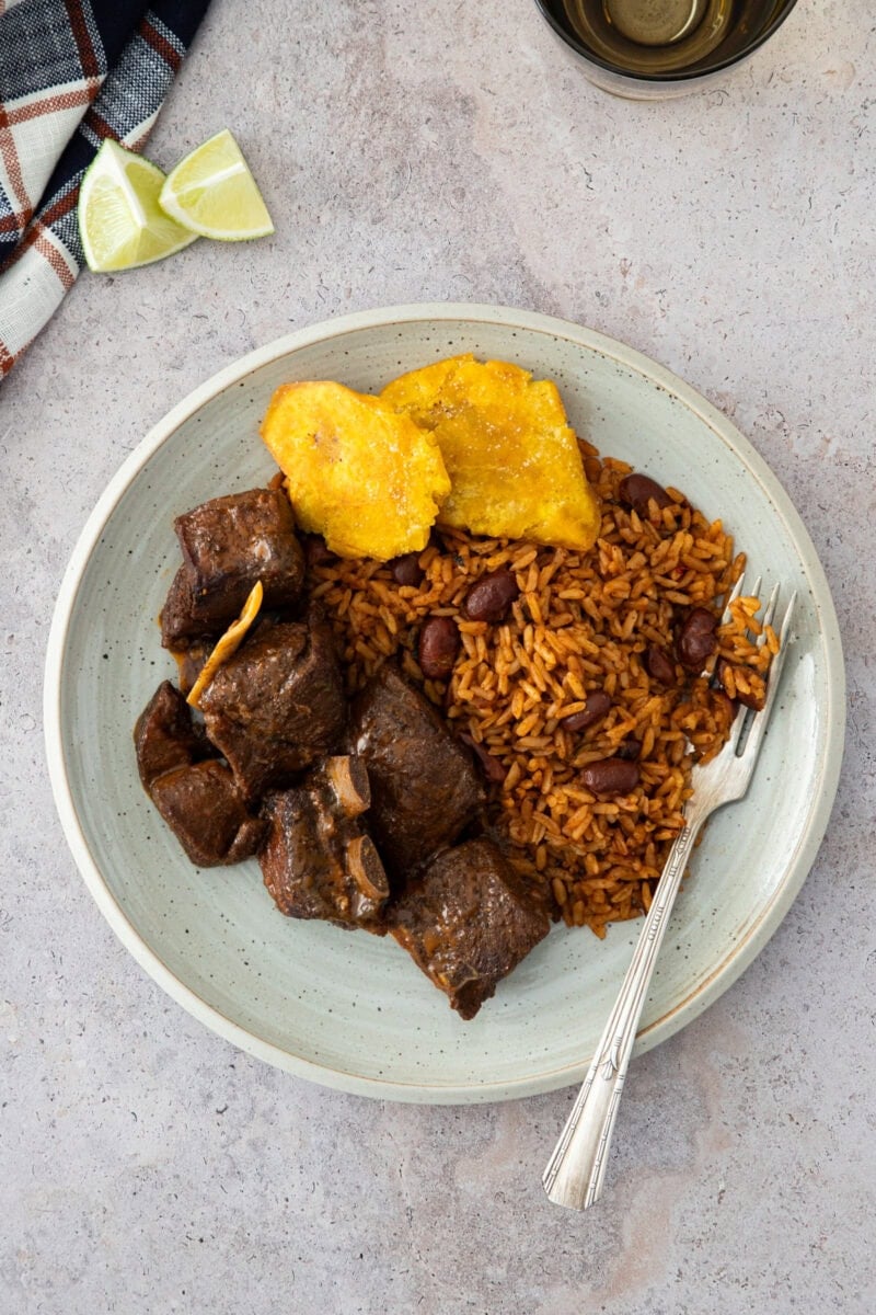 Plate of Dominican stewed goat served with moro rice and fried tostones.