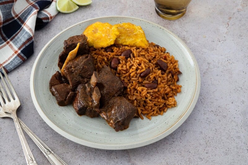 Plate of Dominican stewed goat served with moro rice and fried tostones.