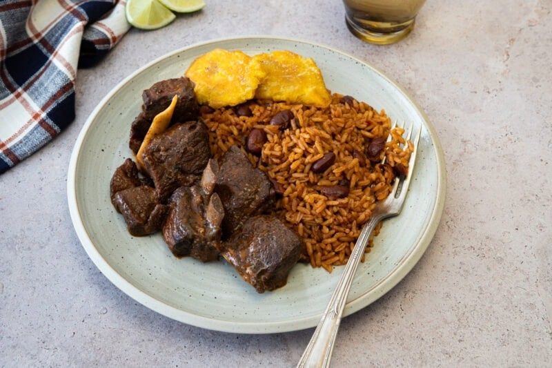 Plate of Dominican stewed goat served with moro rice and fried tostones.