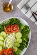 Top view of a green salad arranged with lettuce, cucumbers, tomatoes, and cabbage, served with vinaigrette and forks on a napkin.